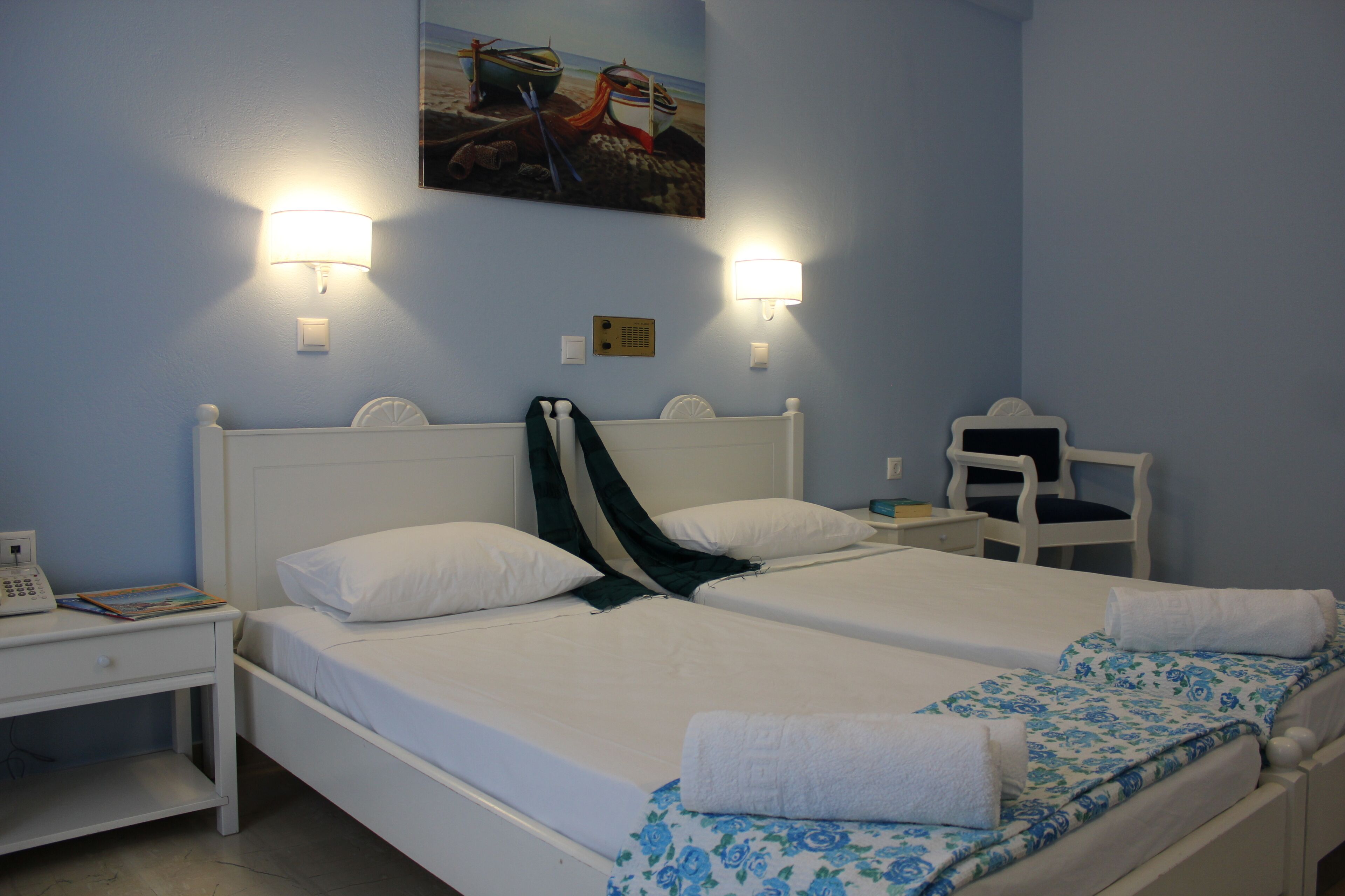 Una cama doble con sábanas blancas, una mesita de noche con lámpara y una silla.