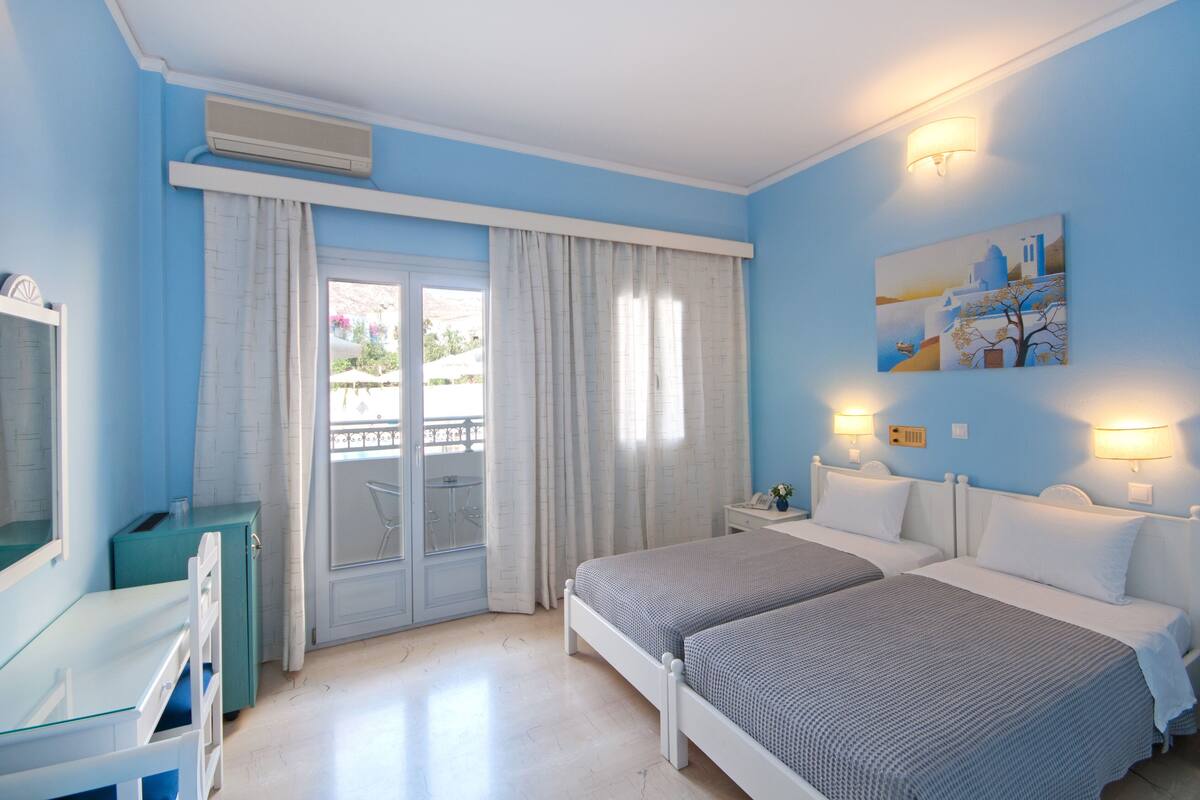 A hotel room with two beds, a desk, a chair, a balcony, and a painting on the wall.