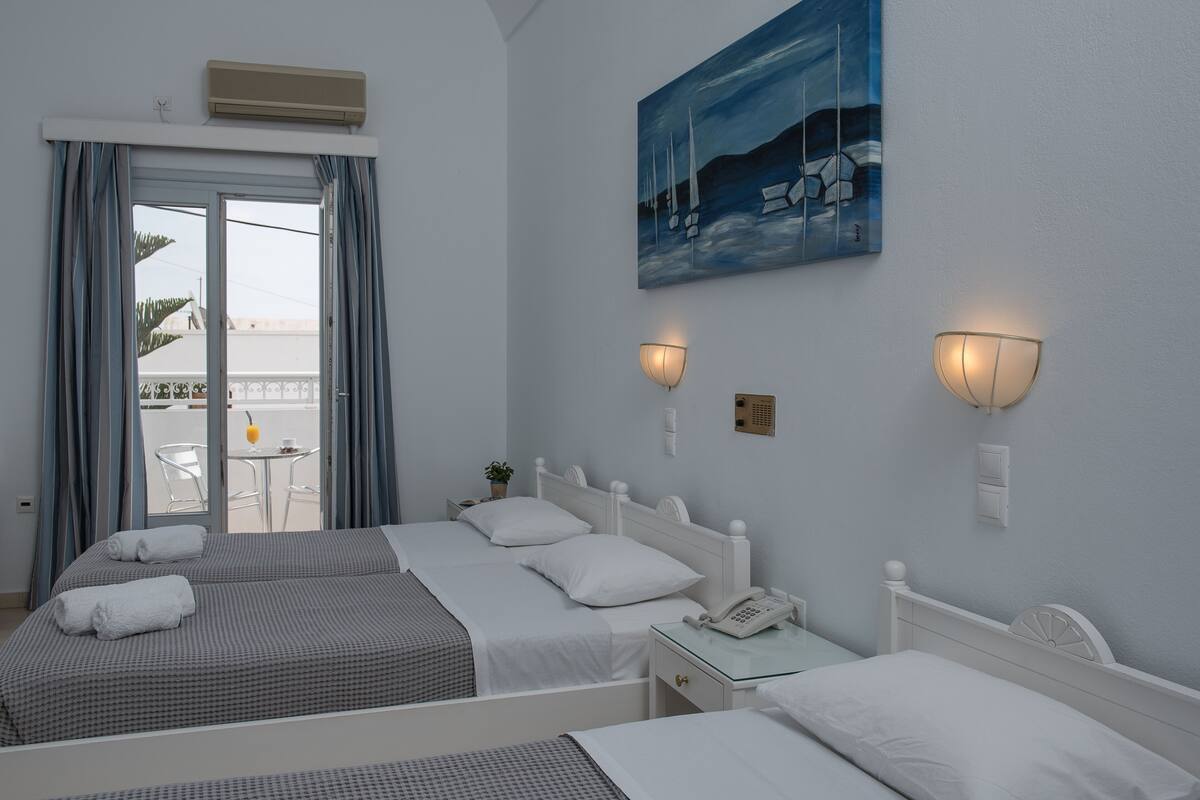 A hotel room with two beds, a balcony with a table and chairs, and a painting on the wall.