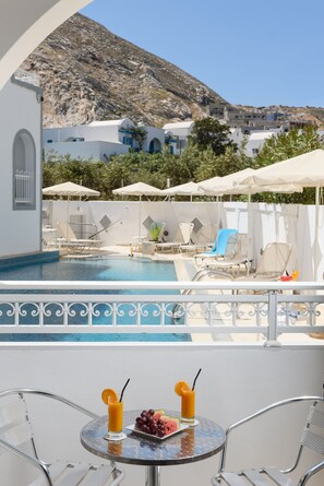 A poolside area with lounge chairs, umbrellas, and a table with drinks and fruit. - Hotel Glaros (Santorini)