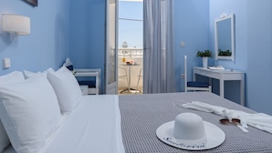 Habitación de hotel con una cama, un escritorio, una silla, un ventanal con cortinas, una mesita y una planta en maceta.