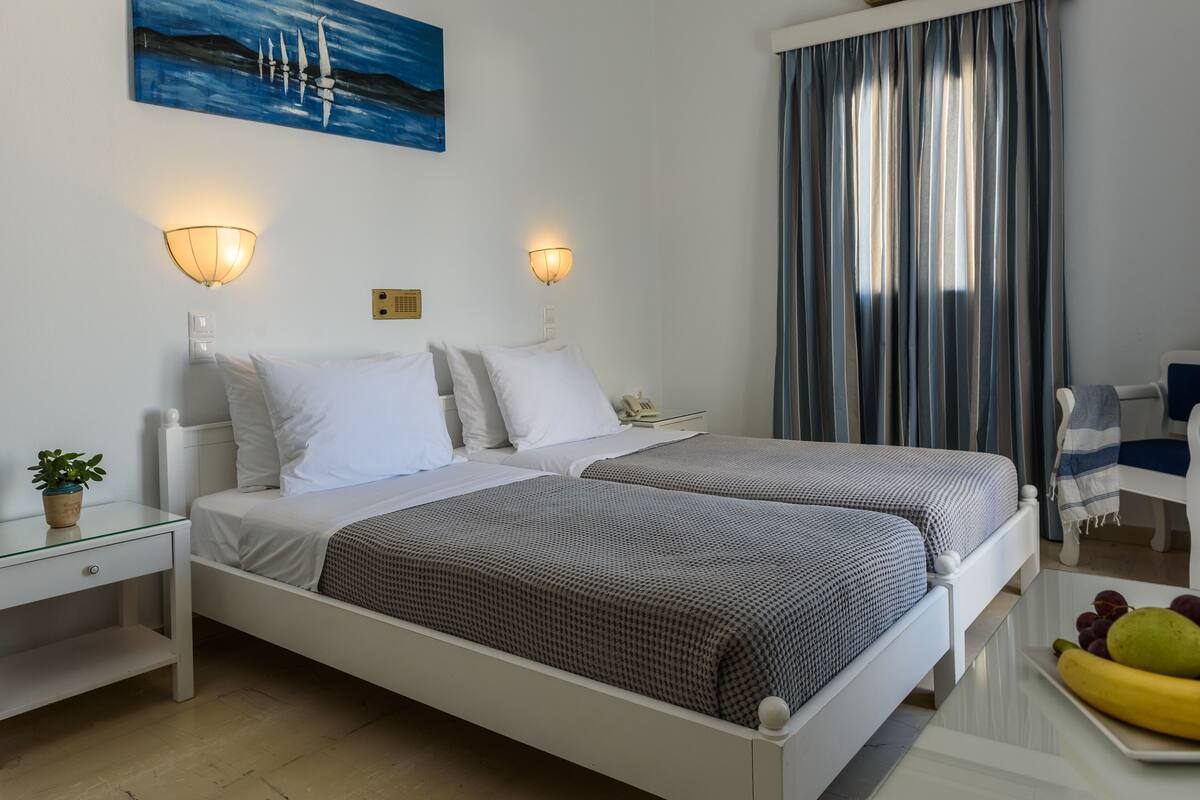 A hotel room with two beds, bedside lamps, a small table with a plant, and a painting on the wall.