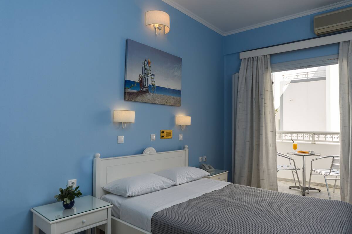 A hotel room with a bed, bedside table, lamp, and a painting of a lighthouse.