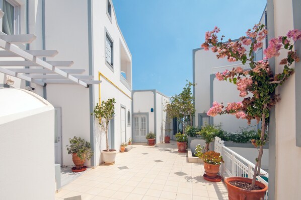 A narrow, tiled courtyard with white buildings, potted plants, and a clear blue sky. - Hotel Glaros (Santorini)