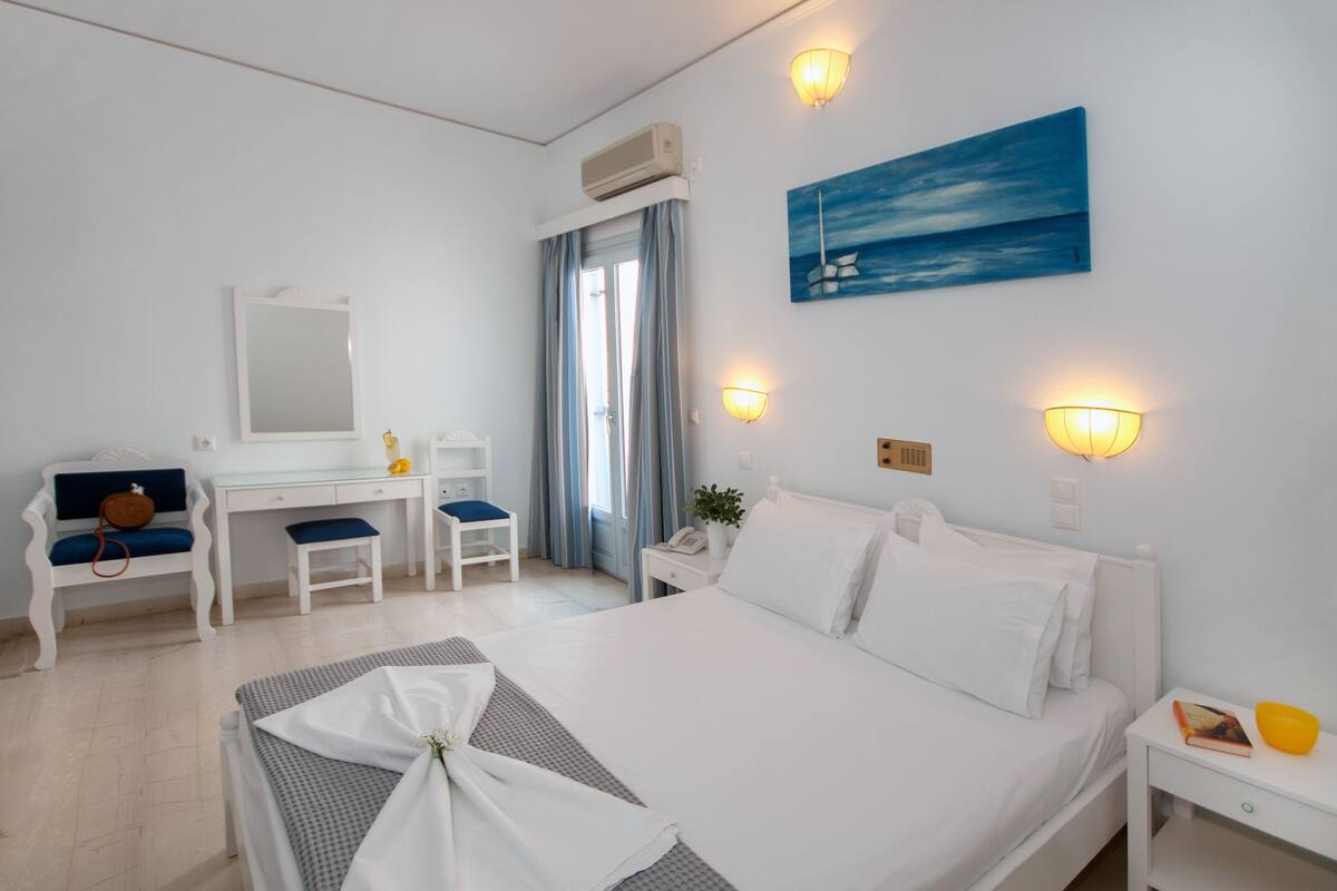 A hotel room with a bed, a desk, a chair, a bedside table, and a window with curtains.