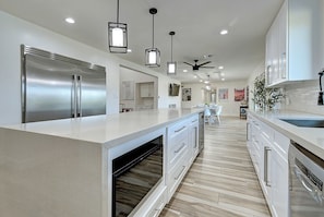 A modern kitchen with a large island, stainless steel appliances, pendant lighting, and a ceiling fan.