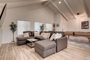 A modern living room with a sectional sofa, a coffee table, and a pool table.