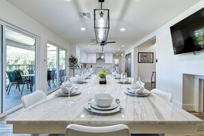 Un espace repas moderne avec une table en marbre dressée pour le repas, de grandes fenêtres et un téléviseur à écran plat fixé au mur.