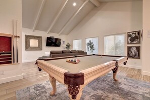 Une table de billard dans une pièce avec un plafond haut, un canapé et des tableaux encadrés accrochés aux murs.