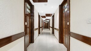 Un long couloir étroit, avec des portes en bois de chaque côté, des murs blancs et un sol carrelé.