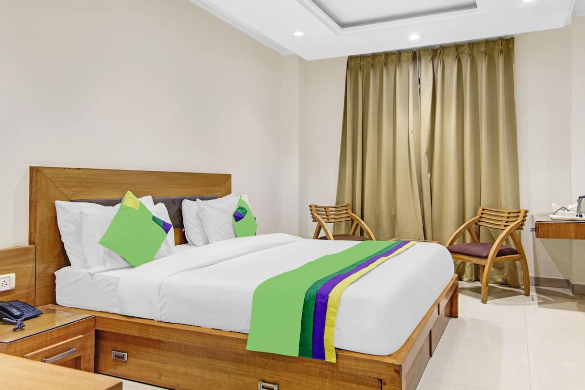 Habitación de hotel con una cama, dos sillas de madera, un escritorio con un hervidor y un espejo.