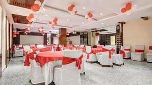 Une salle de banquet avec des tables rondes recouvertes de nappes blanches et ornées de rubans rouges, des chaises avec des housses blanches et des rubans rouges, et un plafond décoré de ballons rouges et blancs.