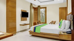 Une chambre d’hôtel moderne dotée d’un grand lit, d’un téléviseur à écran plat fixé au mur, d’une table de chevet en bois, d’un bureau avec un téléphone et d’une fenêtre avec des rideaux.