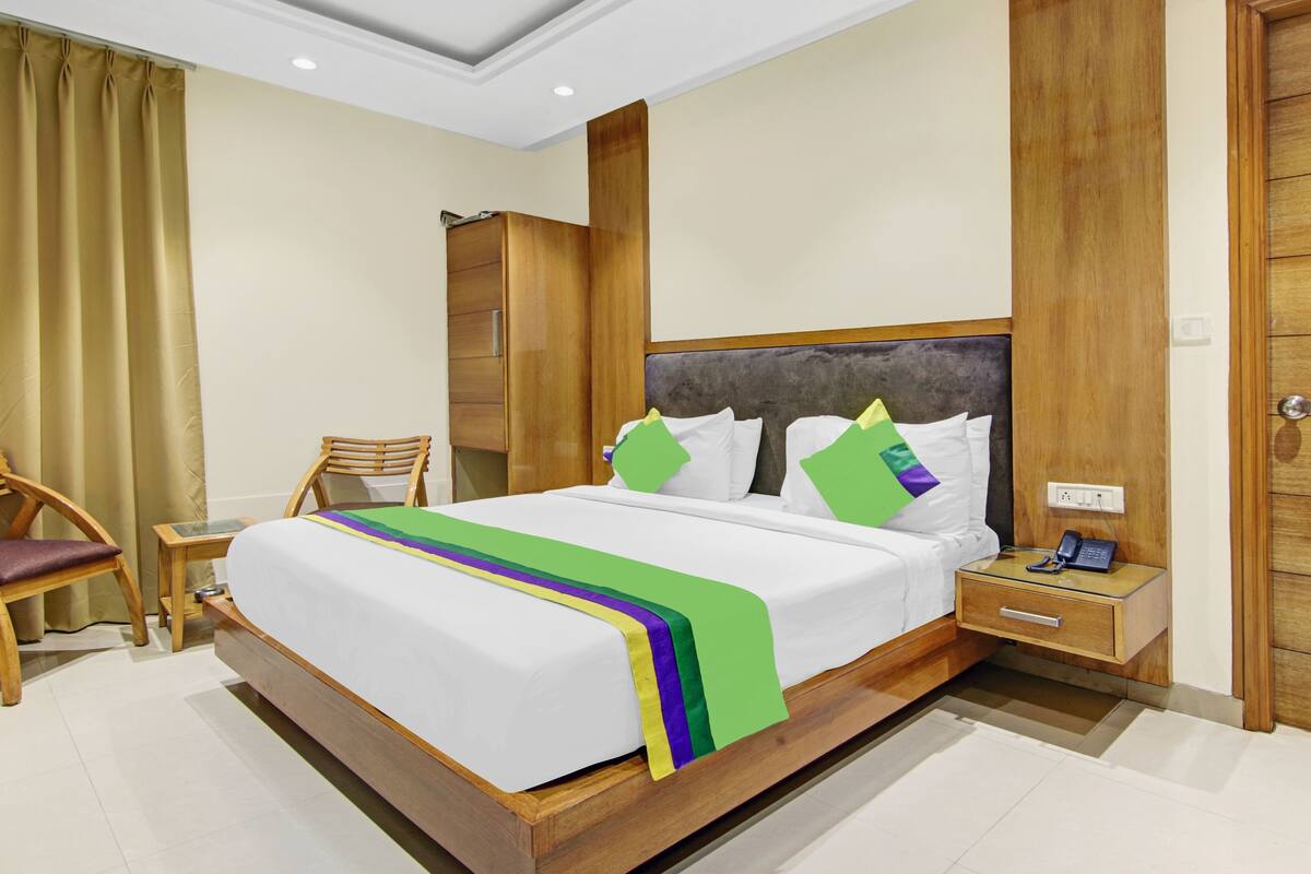Una habitación de hotel con una cama de madera, una mesita de noche con teléfono, un armario de madera y una silla.