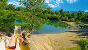 A water slide with two people at the end, surrounded by greenery and a body of water. - La Roque d'Anthéron - Mobil-home - 6 pers - 3 bdrms - Swimming pool (La Roque-d'Anthéron)