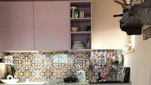 Una cucina compatta con forno integrato, uno sgabello di legno e una sedia colorata.