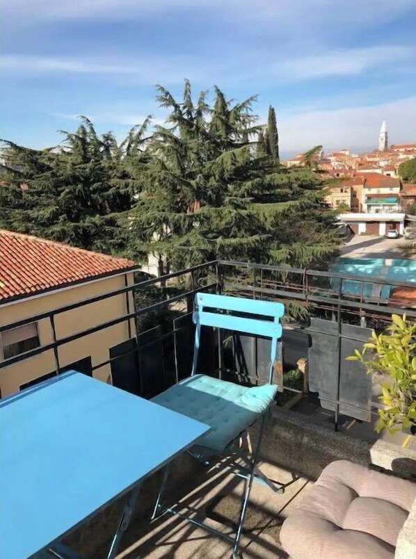 A rooftop terrace with a blue table and chairs, a pool, and a view of trees and buildings.