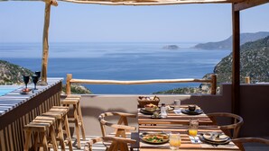 A terrace with wooden furniture and a table set for a meal, overlooking a coastal view with the sea and distant hills. - SWIM UP SUITE with direct access to the infinity pool and stunning sea view (Alonissos)