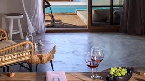 A hotel room with a bed, a wooden table with a book, glasses, and grapes, and a view of the sea and a pool. - SWIM UP SUITE with direct access to the infinity pool and stunning sea view (Alonissos)