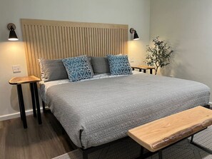 A modern bedroom with a large bed, two bedside tables, a bench, and a wall-mounted lamp. - Mallard House -Peaceful cabin-retreat-like setting (Stratford)