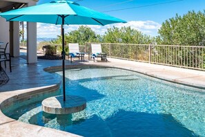 A swimming pool with a curved design, surrounded by lounge chairs and a fence.