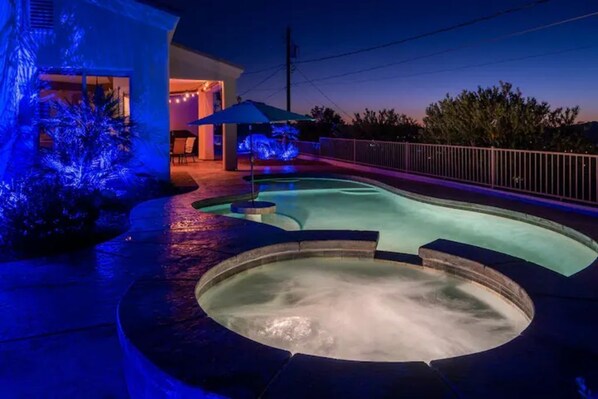 A swimming pool with a hot tub, surrounded by a deck with a railing.