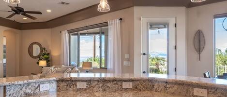 A kitchen with a granite countertop, pendant lighting, a ceiling fan, and a view through a large window.