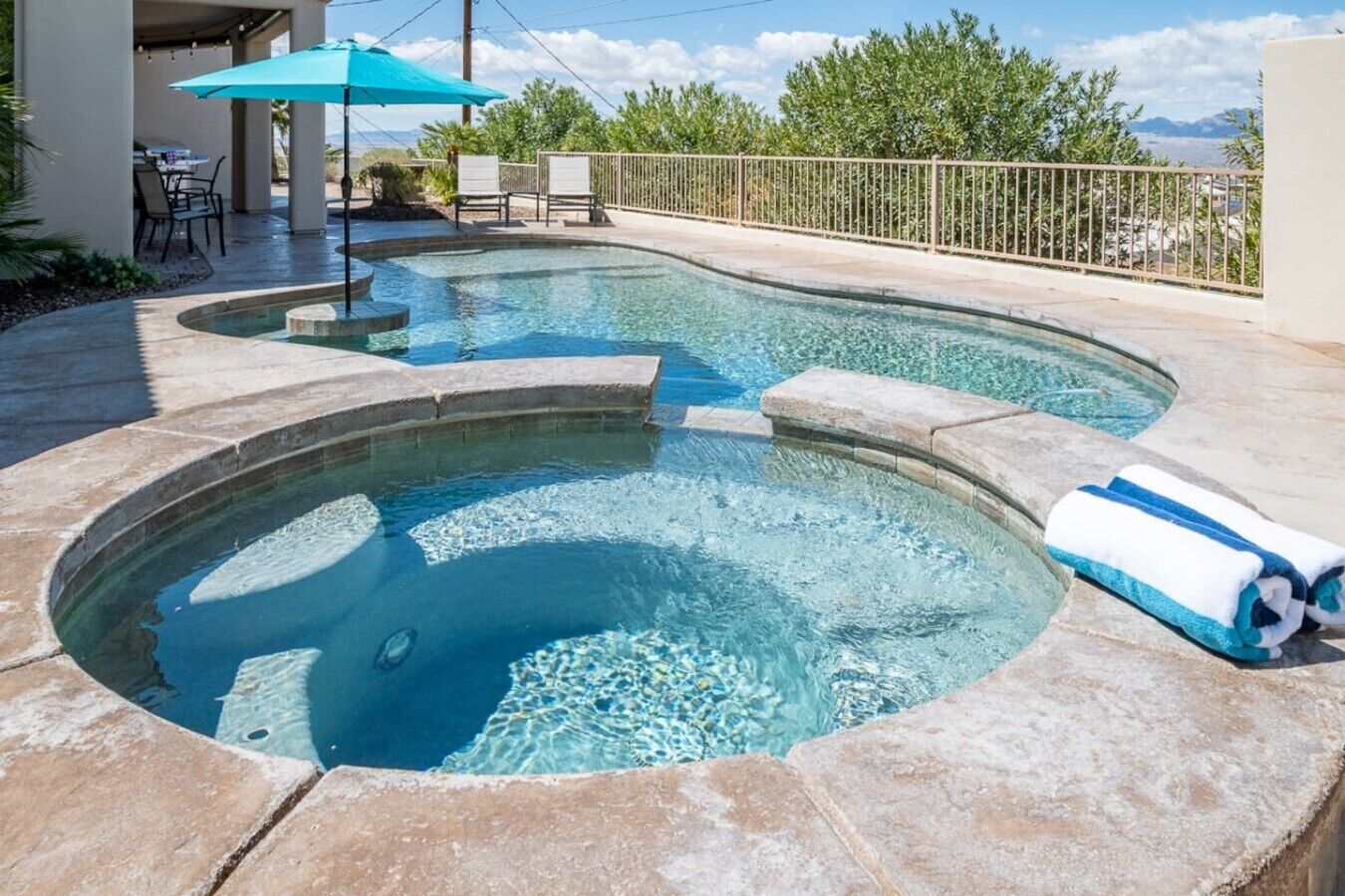 A swimming pool with a stone edge, a lounge area with chairs, and a view of the mountains.