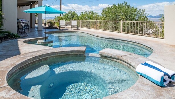 A swimming pool with a stone edge, a lounge area with chairs, and a view of the mountains. - Lake View Oasis Pool/Spa+Boat Garage+Ice Machine (Lake Havasu City)