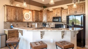 A kitchen with wooden cabinets, a central island with stools, a microwave, and a refrigerator. - Lake View Oasis Pool/Spa+Boat Garage+Ice Machine (Lake Havasu City)