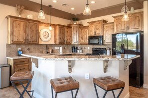 A kitchen with wooden cabinets, a central island with stools, a microwave, and a refrigerator. - Lake View Oasis Pool/Spa+Boat Garage+Ice Machine (Lake Havasu City)