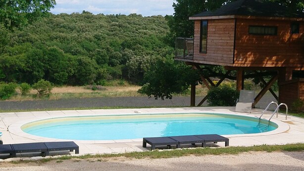 Una piscina con sillas de descanso, una terraza de madera y vistas a un área boscosa.