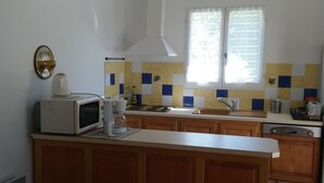 Una cocina con una isla de madera, sillas blancas, un microondas y una ventana con cortinas.