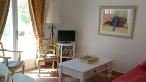 Una sala de estar con una mesa blanca, un sofá rojo, un televisor sobre un mueble blanco y un cuadro en la pared.