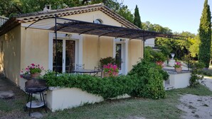 Una casa pequeña de un solo piso con techo de tejas, un porche cubierto con una parrilla y plantas en macetas.