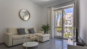 A modern living room with a sofa, coffee table, and a large window with a view of buildings and palm trees.