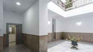 A spacious lobby with a high ceiling, a central planter with plants, and a visible elevator.
