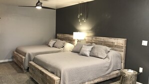 Et soveværelse med to senge, en loftsvifter, en væglampe og et natbord i træ.