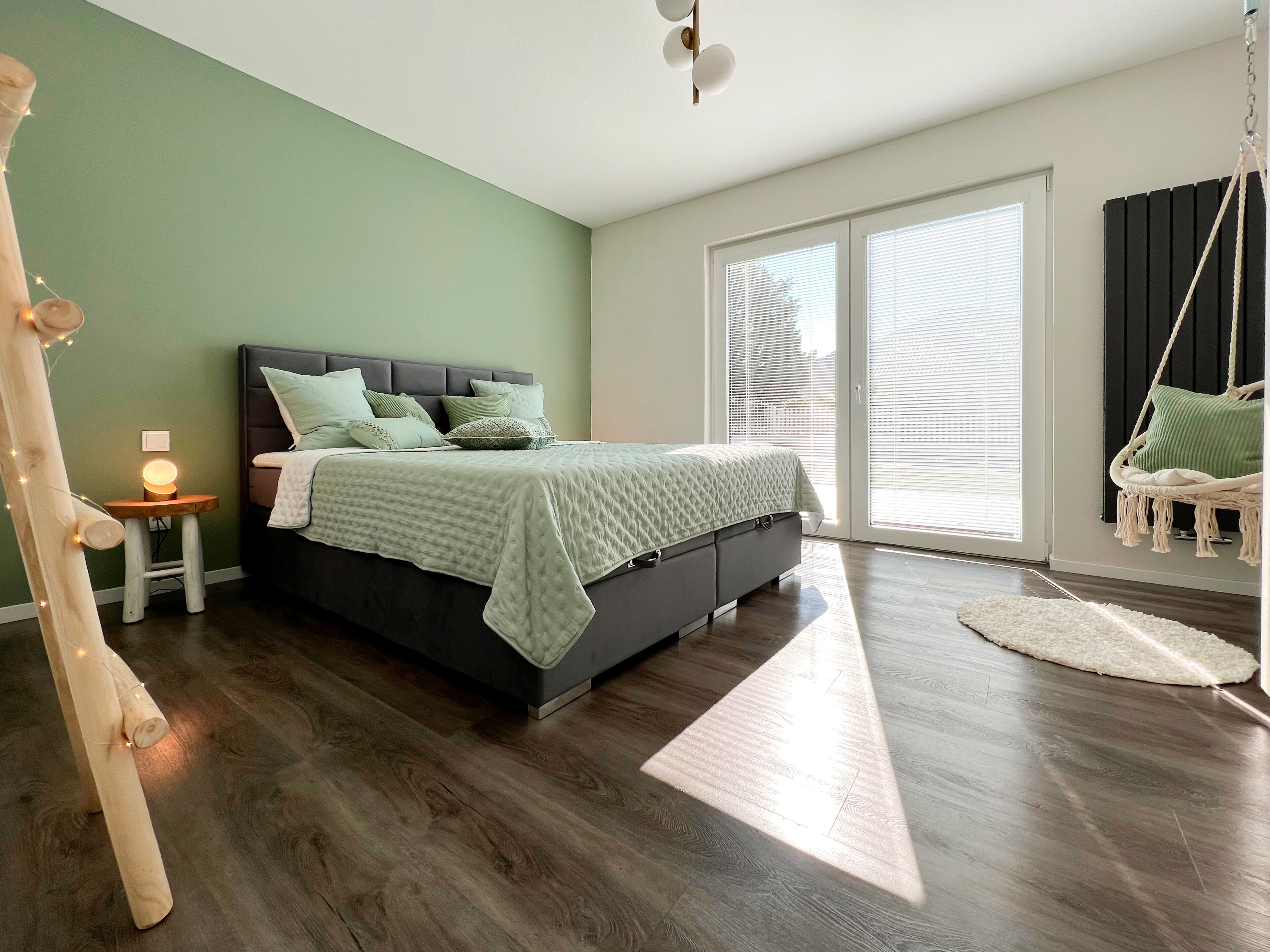 Un dormitorio con cama, mesita de noche, silla colgante y vistas al exterior.