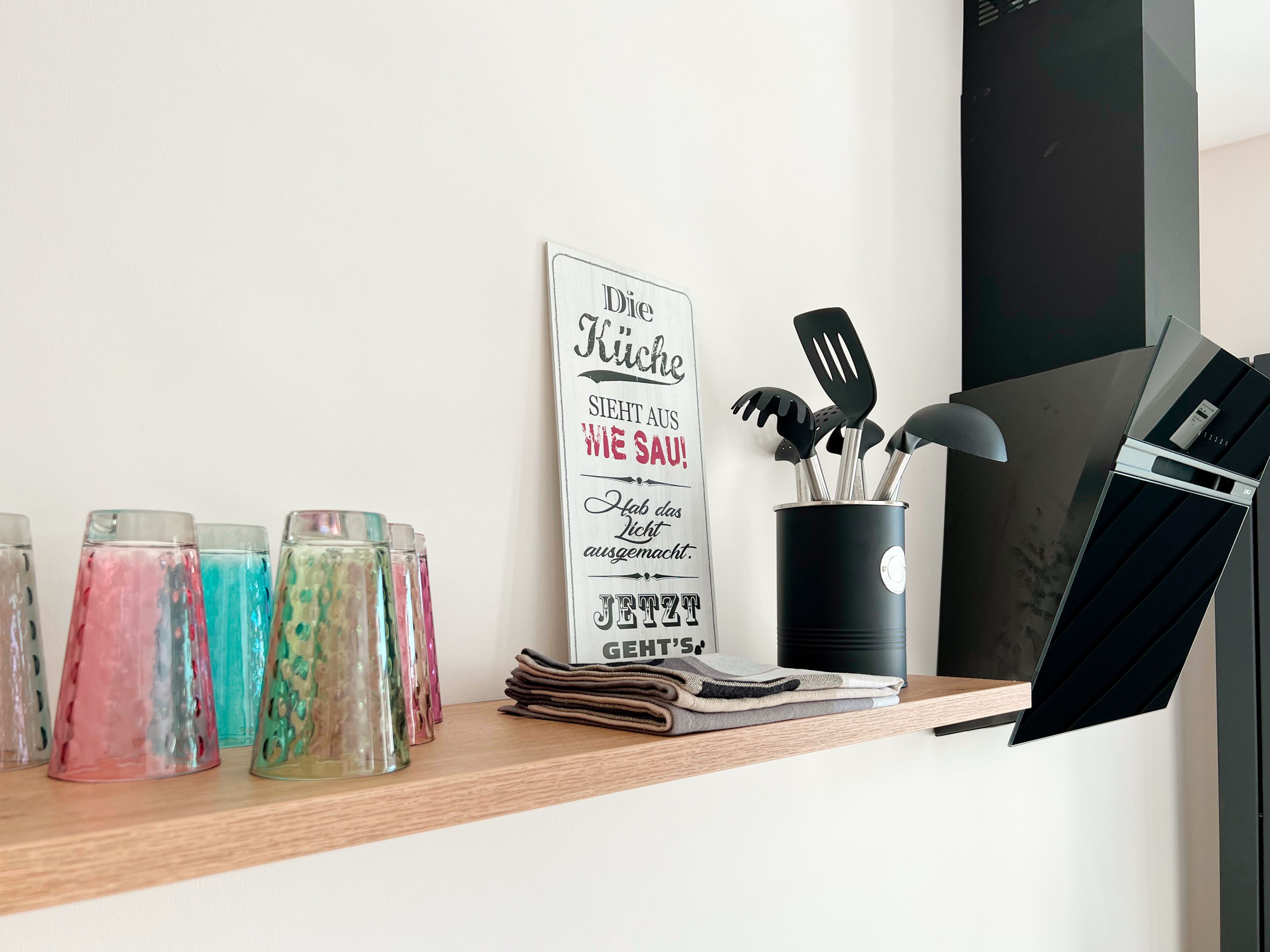 A kitchen counter with a sign, a stack of towels, and a container with kitchen utensils.