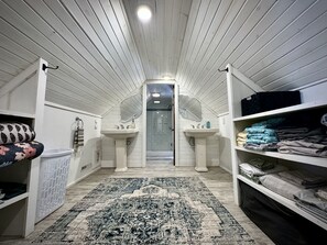 Une petite chambre mansardée avec deux lavabos blancs, un grand miroir et un tapis à motifs.