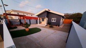 A residential area with a paved driveway, a red pergola, and several potted plants.