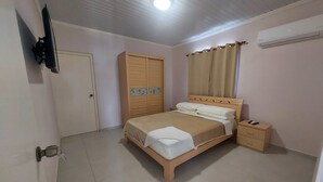 A bedroom with a bed, a wardrobe, a nightstand, a television, and an air conditioning unit.
