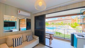 A modern living room with a sofa, TV, and a balcony with a pool view.
