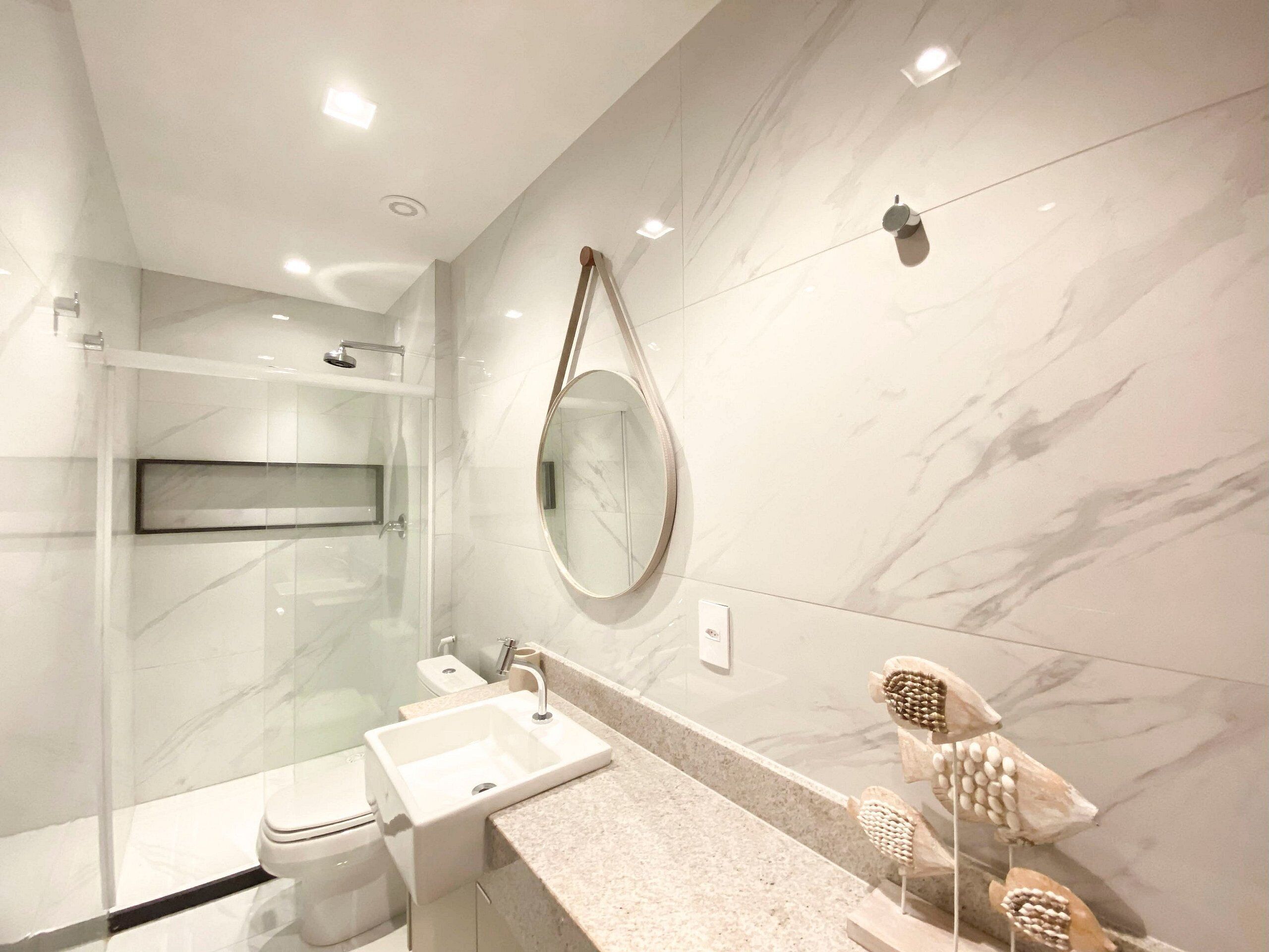 A modern bathroom with a glass shower enclosure, a sink, a toilet, and a marble wall.