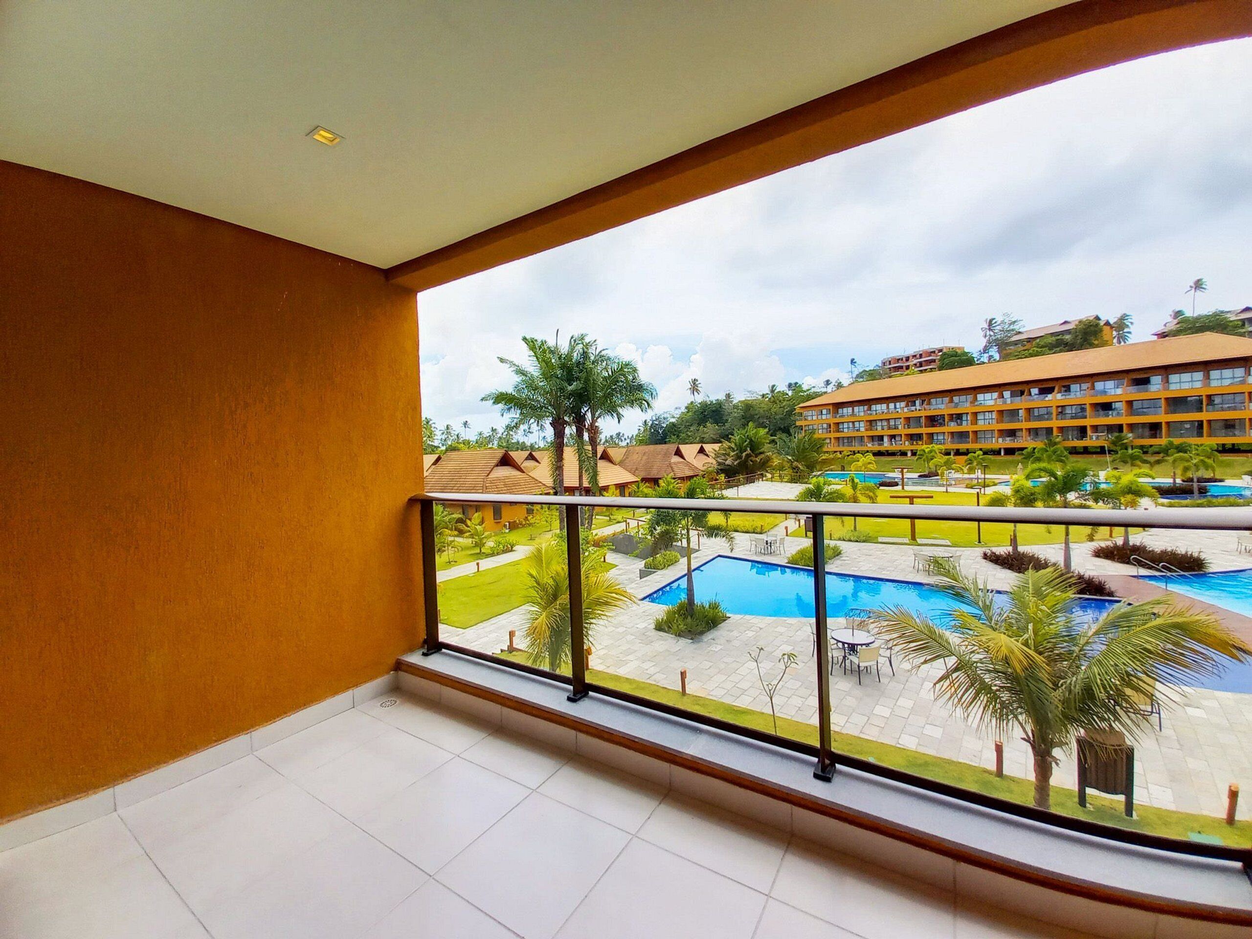 A balcony with a view of a hotel courtyard, including a swimming pool and palm trees.