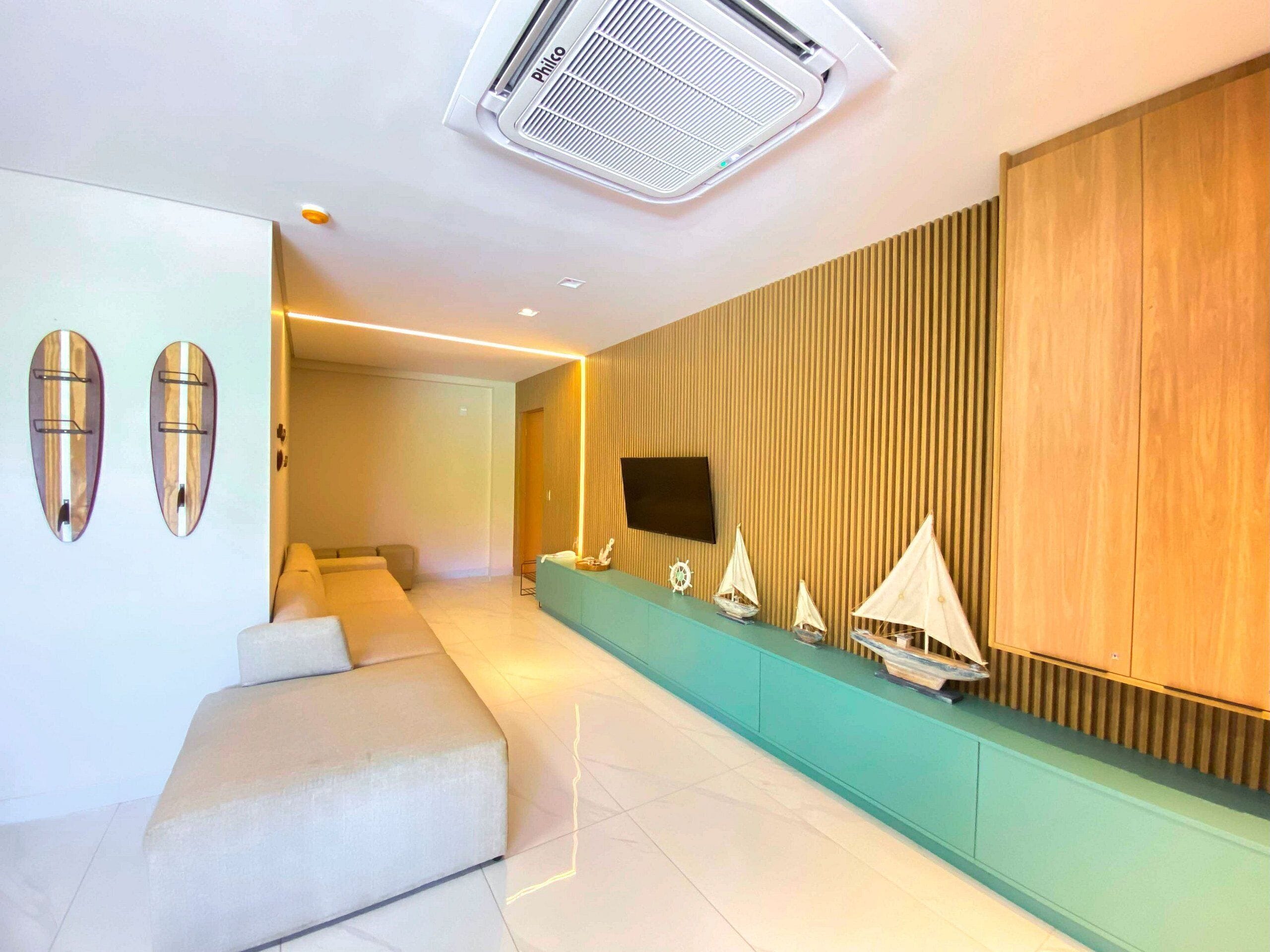 A modern living room with a sofa, a flat-screen TV mounted on a wooden wall, and a series of small sailboats displayed on a shelf.