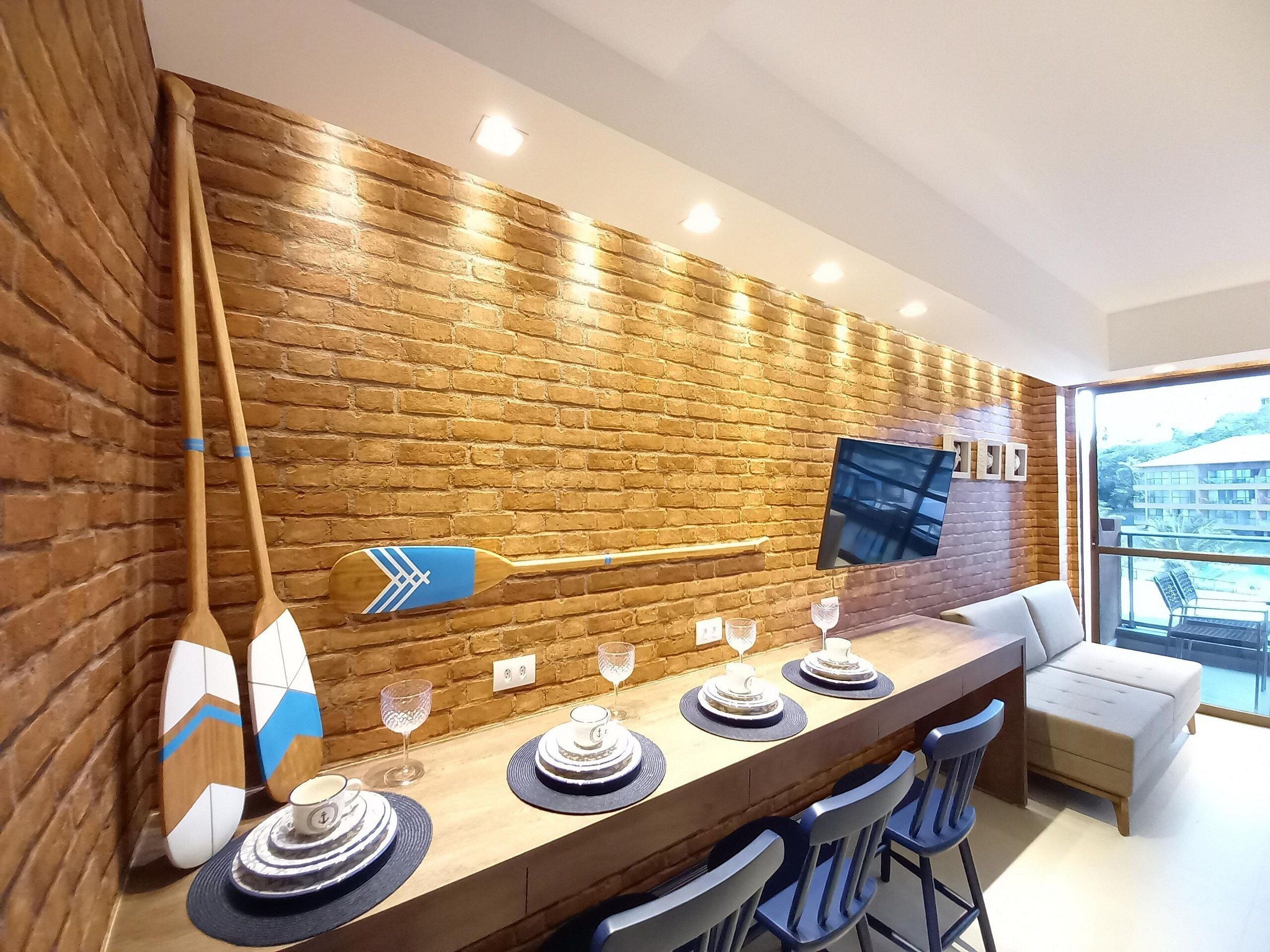 Un espace repas moderne avec un mur en briques, une table à manger en bois, des chaises et un téléviseur fixé au mur.