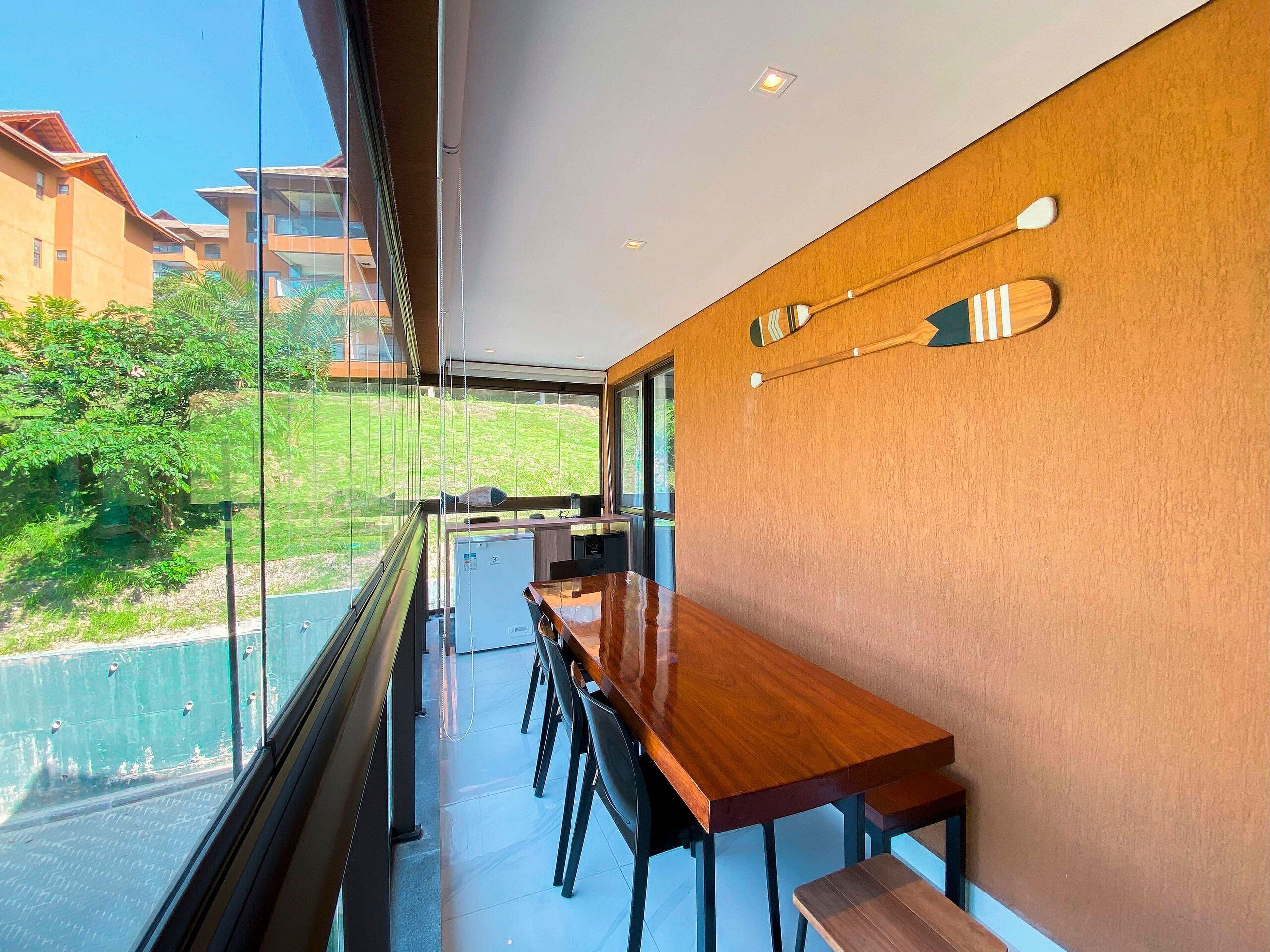 A modern kitchen with a wooden countertop and bar seating, large windows, and a view of greenery and buildings outside.