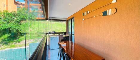 A modern kitchen with a wooden countertop and bar seating, large windows, and a view of greenery and buildings outside.